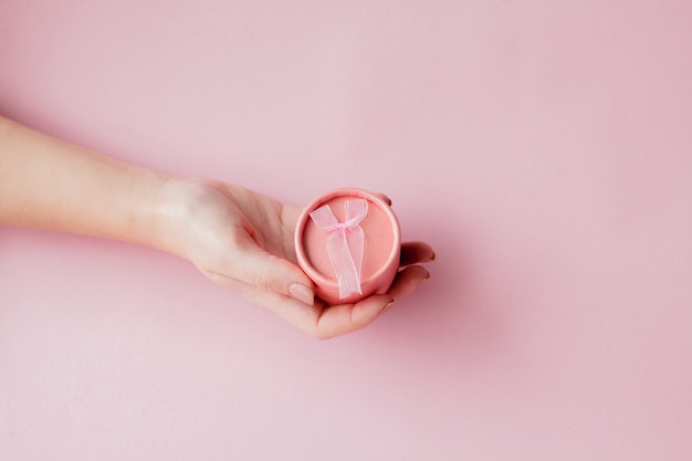 Coffret rose rond dans les mains des femmes sur fond rose. Concept festif pour la Saint-Valentin, la fête des mères ou l'anniversaire