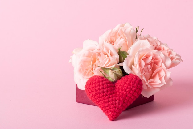 Coffret rose avec des roses et un coeur rouge tricoté sur fond rose clair avec une place pour le texte