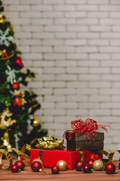 Coffrets cadeaux colorés avec noeud papillon en ruban de couleur vive placé sur le coin d'une table en bois devant un magnifique sapin de Noël entièrement décoratif et un mur de briques en arrière-plan flou.