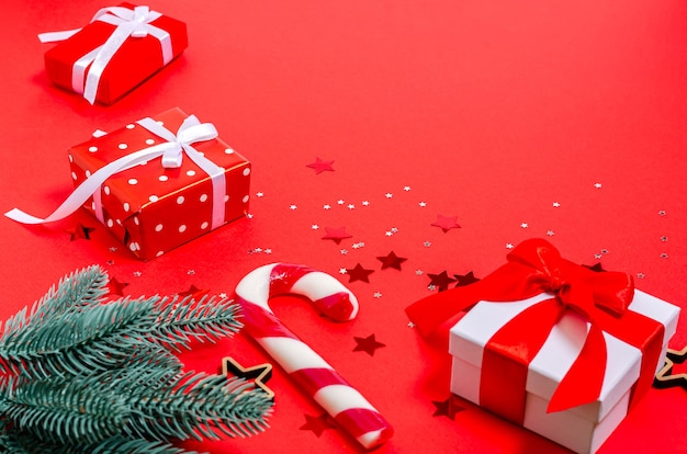 Coffrets cadeaux, jouets de Noël, branches de sapin, étoiles en bois, cannes au caramel sur fond rouge. Bannière, forme de carte postale. Copiez l'espace, pose à plat. Nouvel An, Noël, vacances, 2021. Vue d'en haut.