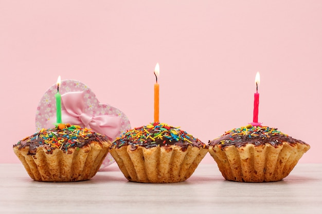 Coffrets Cadeaux Et Muffins D'anniversaire Savoureux Avec Glaçage Au Chocolat Et Caramel, Décorés De Bougies Festives Allumées Sur Fond Bois Et Rose. Notion De Joyeux Anniversaire.