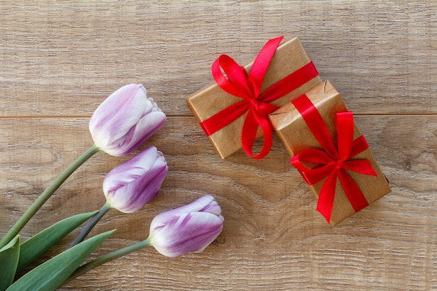 Coffrets cadeaux avec des rubans rouges et de belles tulipes sur les planches de bois. Vue de dessus. Concept de donner un cadeau en vacances.
