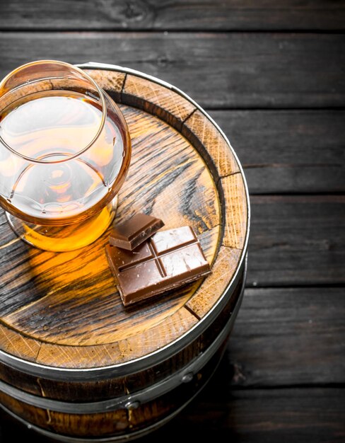 Photo cognac dans un verre avec du chocolat sur un tonneau