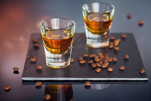 Cognac ou liqueur, grains de café et épices sur une table en verre