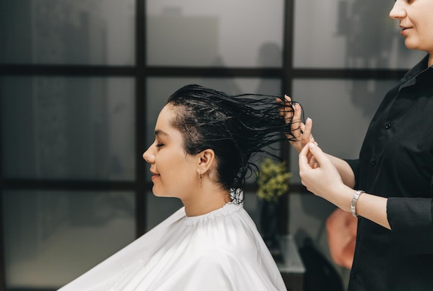 Le coiffeur applique le gel sur les cheveux d'une femme dans un salon de beauté