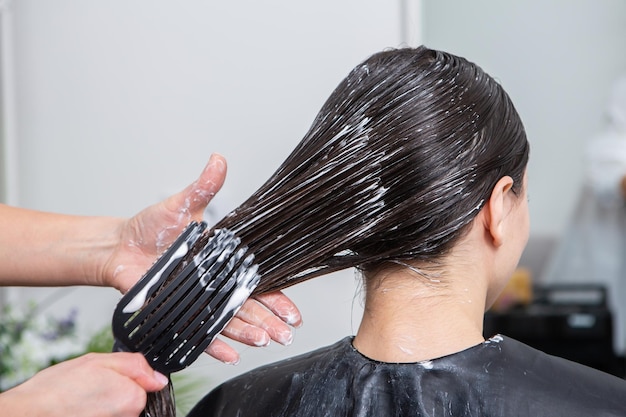 Le coiffeur applique un masque capillaire sur les cheveux noirs raides.