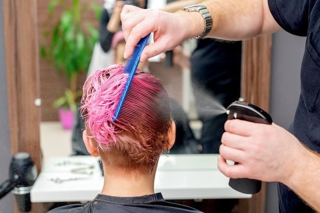 Le coiffeur arrose de l'eau sur les cheveux.