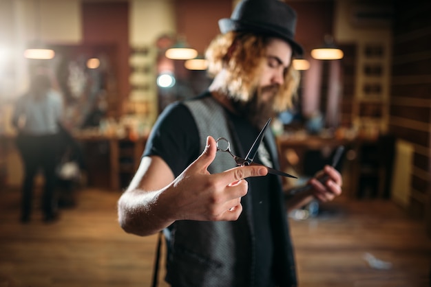 Coiffeur barbu brutal en chapeau pose avec des ciseaux à la main