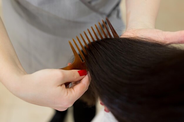 Coiffeur de cheveux longs bruns brillants et sains forts peignant les cheveux du client