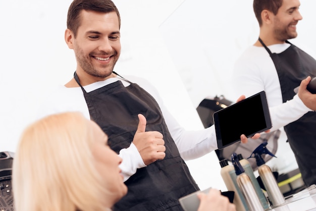 Le coiffeur choisit une coupe de cheveux pour femme sur une tablette.