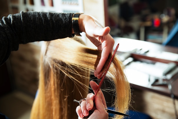 Coiffeur avec des ciseaux et peigne les cheveux mignons à la jeune femme.