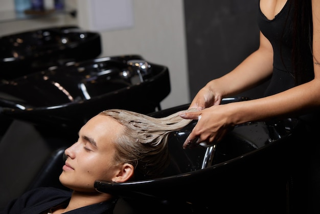 Photo coiffeur coiffeur laver les cheveux du client jeune homme se détendre dans un salon de beauté coiffure