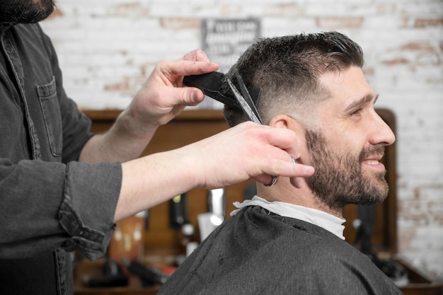 Coiffeur coupant les cheveux avec des ciseaux à un beau jeune homme Photographie de haute qualité