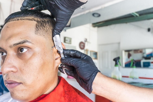 Coiffeur coupant les cheveux d'un client latin à l'aide d'un rasoir manuel