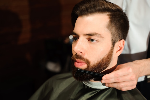 Le coiffeur coupe les cheveux et la barbe de l'homme dans le salon de coiffure