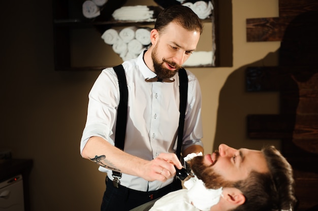 Le coiffeur coupe les cheveux et la barbe de l'homme dans le salon de coiffure