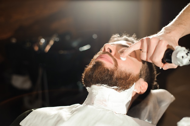 Le coiffeur coupe les cheveux et la barbe de l'homme dans le salon de coiffure