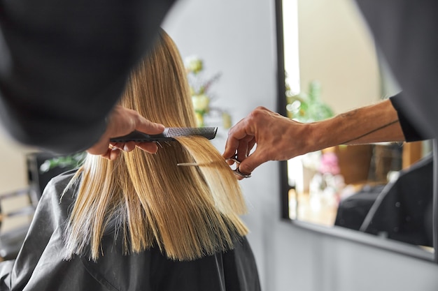 Le coiffeur coupe les cheveux d'une femme blonde est un salon