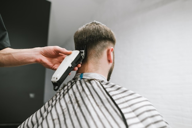 Le coiffeur coupe le client La main avec une tondeuse rase les cheveux de l'arrière de la tête Utilisation de la tondeuse