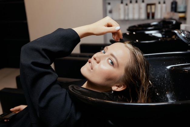 Le coiffeur dans le salon de beauté lave les cheveux de ses clients, avant la procédure d'application d'ingrédients de restauration naturels et de vitamines aux cheveux et à la coupe de cheveux.