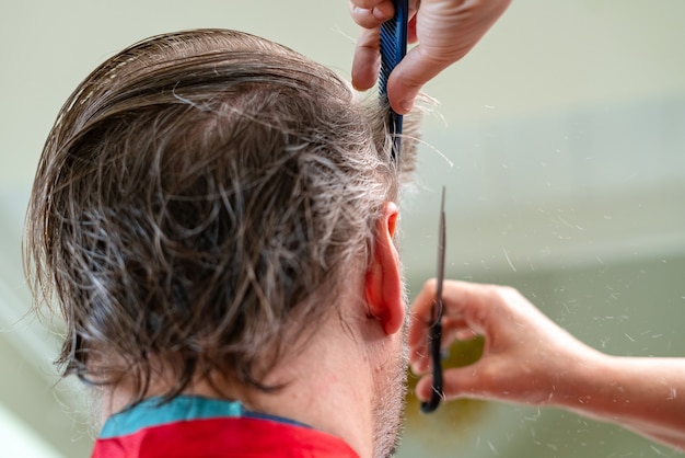 Coiffeur à domicile coupe les cheveux de l'homme à l'intérieur. Femme coupant les cheveux de son mari pendant la quarantaine.