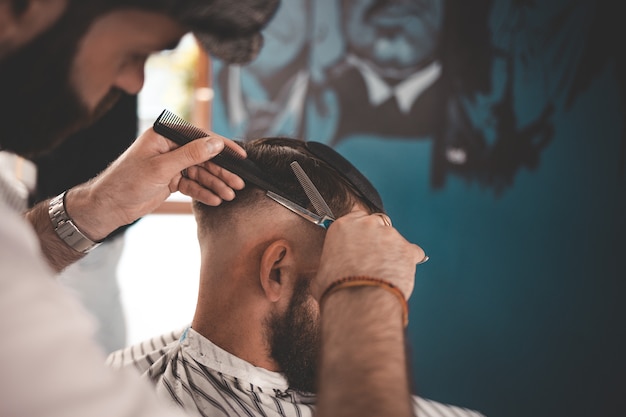 Coiffeur élégant dans une casquette fait une coupe de cheveux