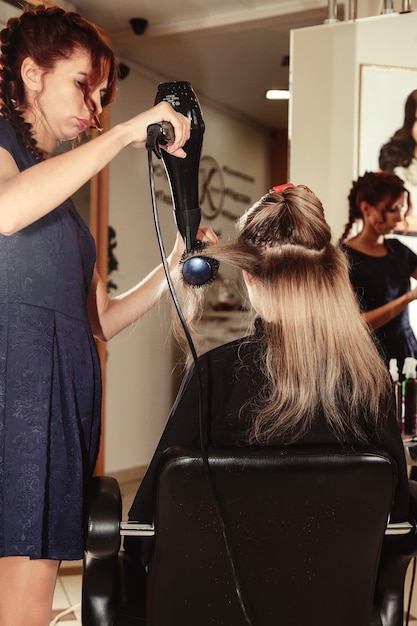 Coiffeur Fait Coiffure Jolie Jeune Femme Dans Un Salon De Beauté. Le Service Client Dans La Salle Intérieure Crée Une Image Incroyable. Assistant De Création De Coiffures De Travail. Concept De Mode De Vie Sain Et De Bien-être