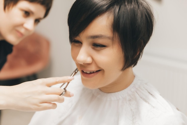 Le coiffeur fait une coupe de cheveux à une femme dans le salon Le coiffeur coupe les cheveux mouillés en se peignant avec un peigne client aux cheveux courts vue arrière