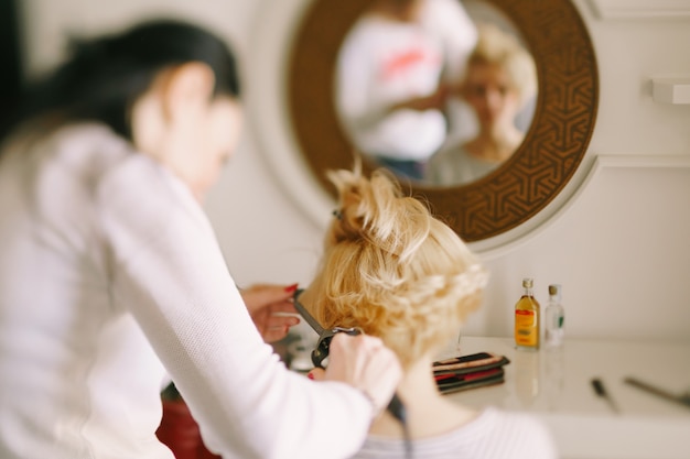 Le coiffeur fait le style de fille avec une vue arrière de plan rapproché de fer à friser