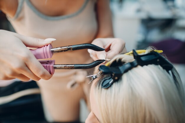 Coiffeur femelle faisant des extensions de cheveux à une jeune femme aux cheveux blonds dans un salon de beauté