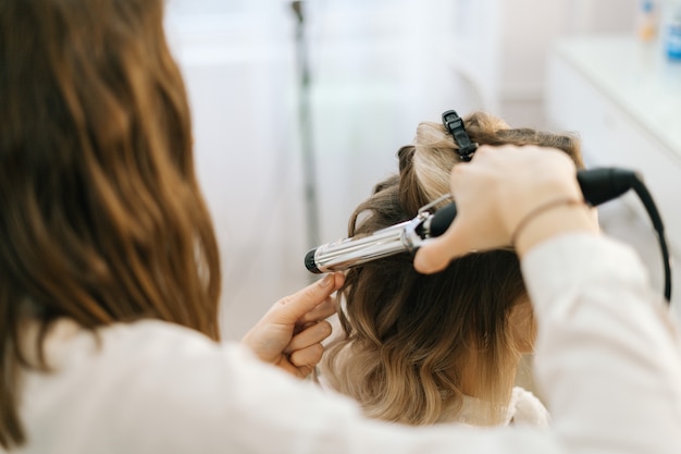 Coiffeur féminin faisant la coiffure pour la jeune femme aux cheveux blonds dans le salon