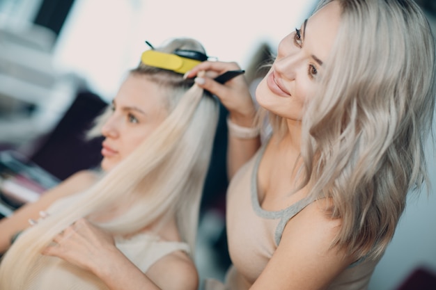 Coiffeur féminin faisant des extensions de cheveux à une jeune femme aux cheveux blonds dans un salon de beauté. Extension de cheveux professionnelle.
