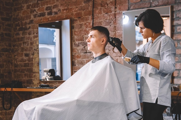 Le coiffeur de femme fait une coupe de cheveux la tête de clients avec une tondeuse électrique dans un salon de coiffure