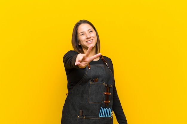 Coiffeur femme souriante et à la recherche de joie heureuse, insouciante et positive, gesticulant ou paix avec une main contre orange