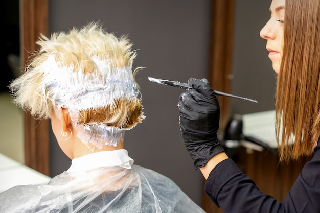 Coiffeur femme teinture cheveux blonds courts d'une jeune femme dans un salon de coiffure