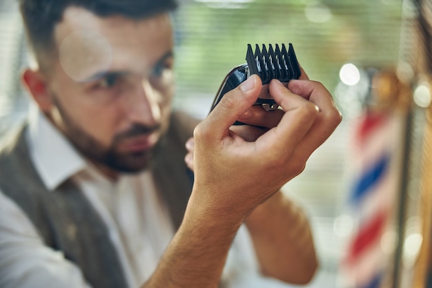 Coiffeur hautement qualifié vérifiant les protections d'une tondeuse électrique et la nettoyant