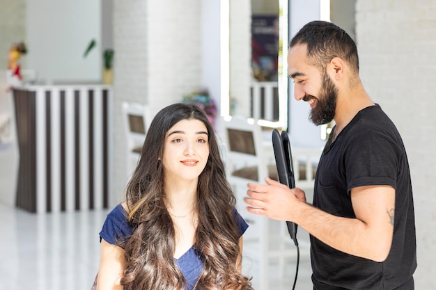 Coiffeur joyeux tenant un sèche-cheveux et regardant son client Photo de haute qualité