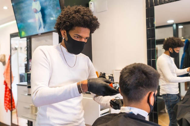 Coiffeur latin avec masque et gants coupant les cheveux du client avec un rasoir