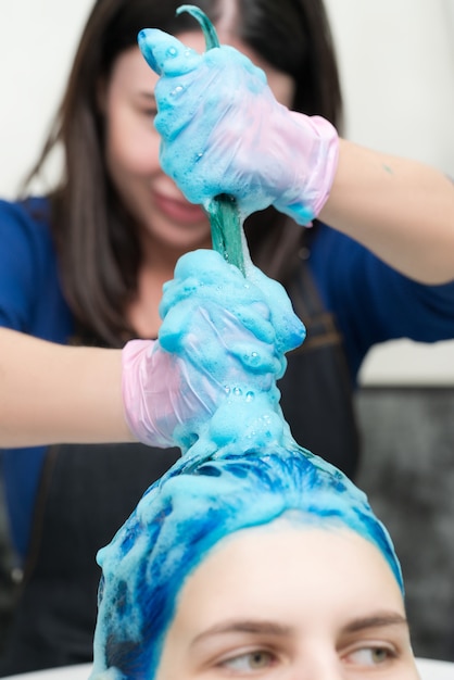 Un coiffeur lave la tête d'une femme avec une couleur de cheveux bleu foncé après le processus de teinture des cheveux dans un salon de beauté p...