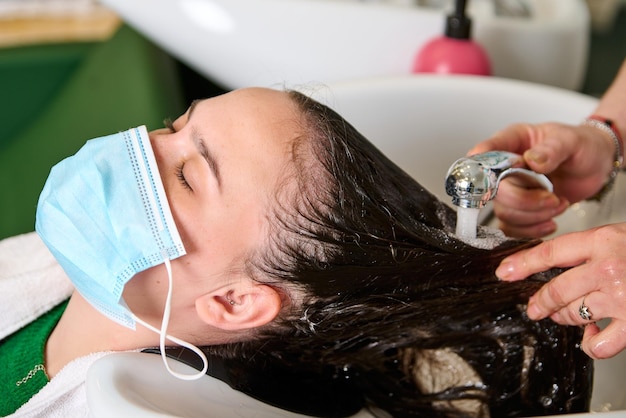 Le coiffeur lave la tête d'une fille brune avec du shampoing dans le salon de beauté