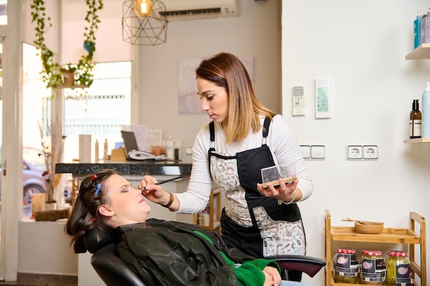 coiffeur maquillant et coiffant une jeune cliente dans un salon de beauté