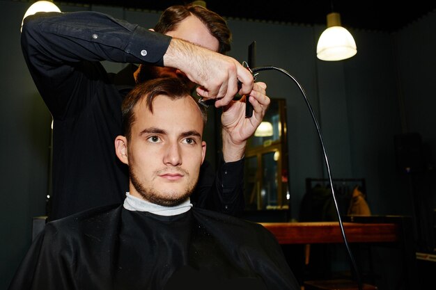 Le coiffeur masculin coupe les tondeuses électriques de client dans le salon de coiffure