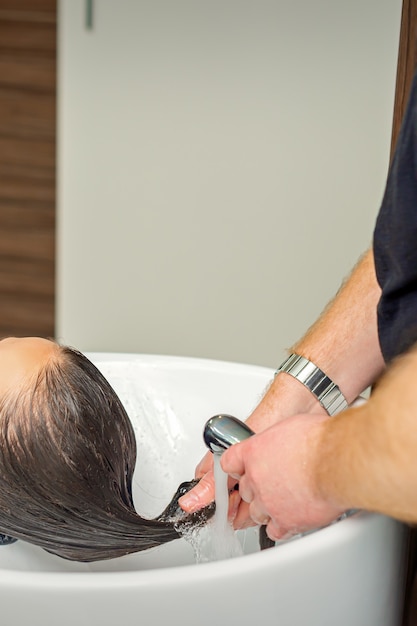 Coiffeur masculin rince les cheveux de la jeune femme dans un salon de coiffure