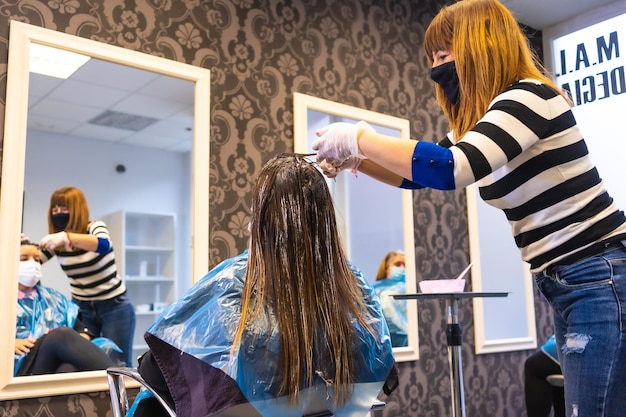 Coiffeur avec un masque appliquant la teinture sur les cheveux gris du client avec un masque