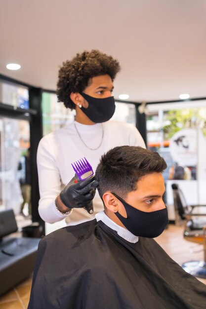 Coiffeur avec masque et gants coupant les cheveux du client avec un rasoir