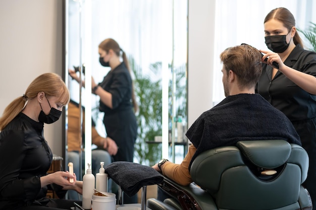 Coiffeur en masque de protection coiffant les cheveux au client