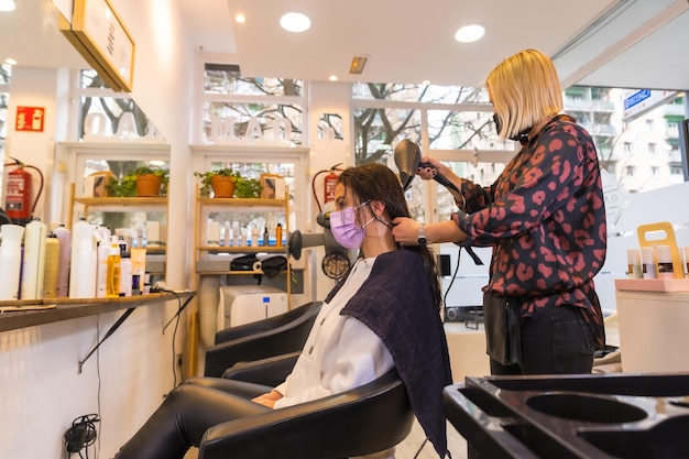 Coiffeur avec masque de protection faciale séchant les cheveux du client avec un sèche-cheveux Mesures de sécurité dans la pandémie de Covid19