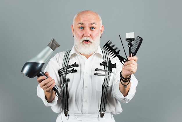 Coiffeur mature barbier en salon de coiffure. Vieux coiffeur étonné excité avec des outils d'équipement de coiffeur.