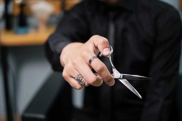 Le coiffeur montre des ciseaux pour couper les cheveux Un coiffeur élégant tient des ciseaux dans sa main Anneaux sur la main