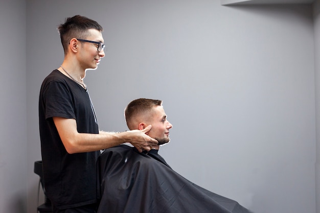 Coiffeur ouzbek coupe un jeune beau mec dans un salon de coiffure, un client masculin est assis dans un salon de beauté et fait une coupe courte